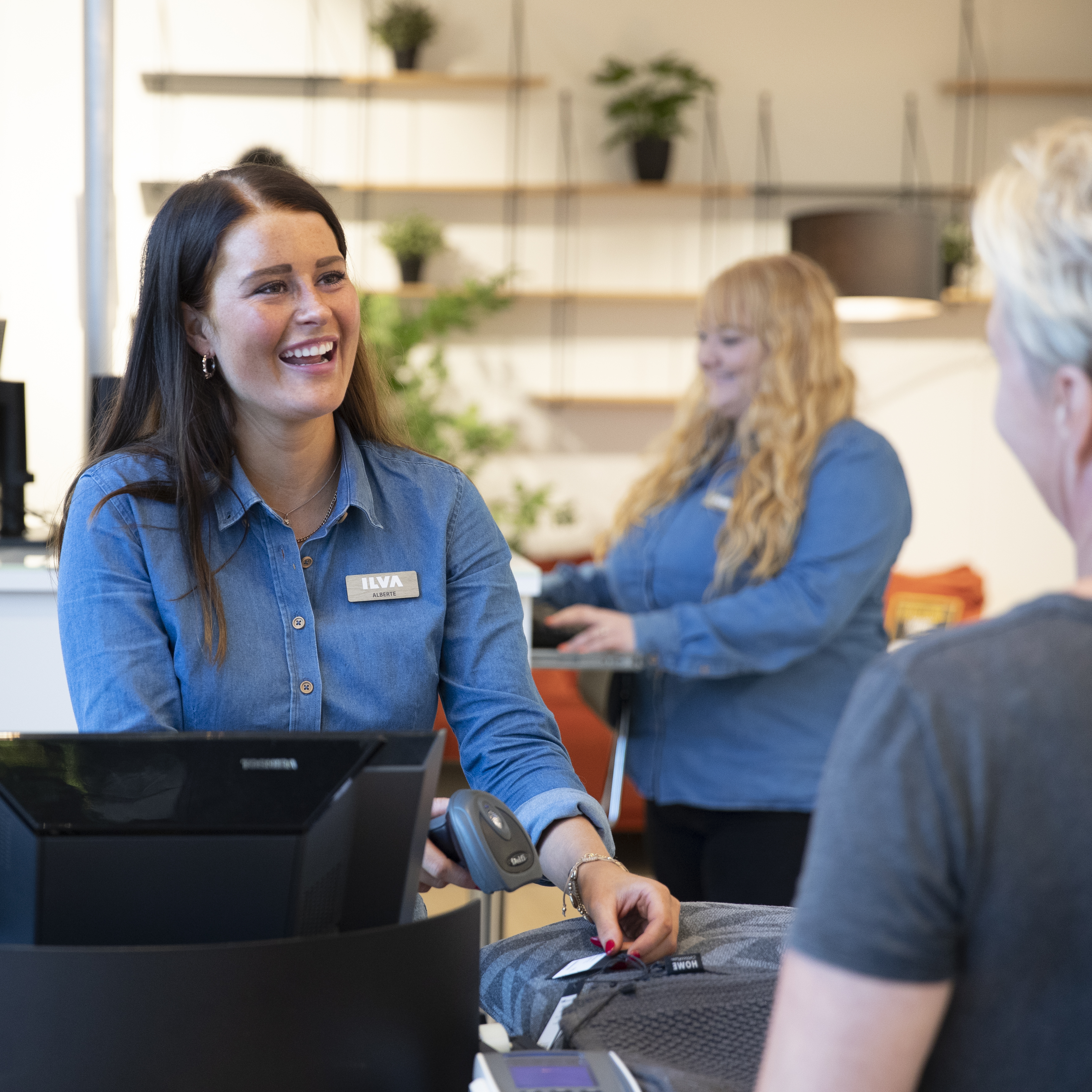 Smilende butiksekspedient i blå skjorte betjener kunde ved kassen