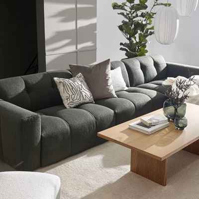 Mørkegrøn modulsofa med puder og et sofabord i lyst træ i en moderne stueindretning.