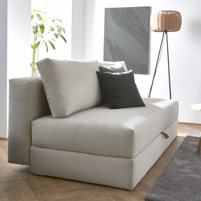 Beige sofa med ribstruktur i et skandinavisk hjem, kompletteret med mørkegrønne puder og et tæppe i gråt.