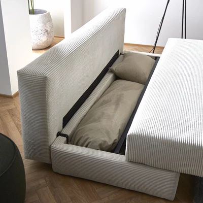 Opbevaringsfunktion under en beige ribbet sofa med plads til puder eller tæpper i et moderne rum.