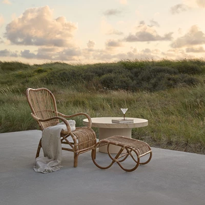 Lænestol i naturrattan med skammel stående på terrasse med naturklitter bagved