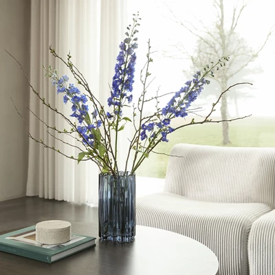 Blå vase med blålige blomster stående på sofabord