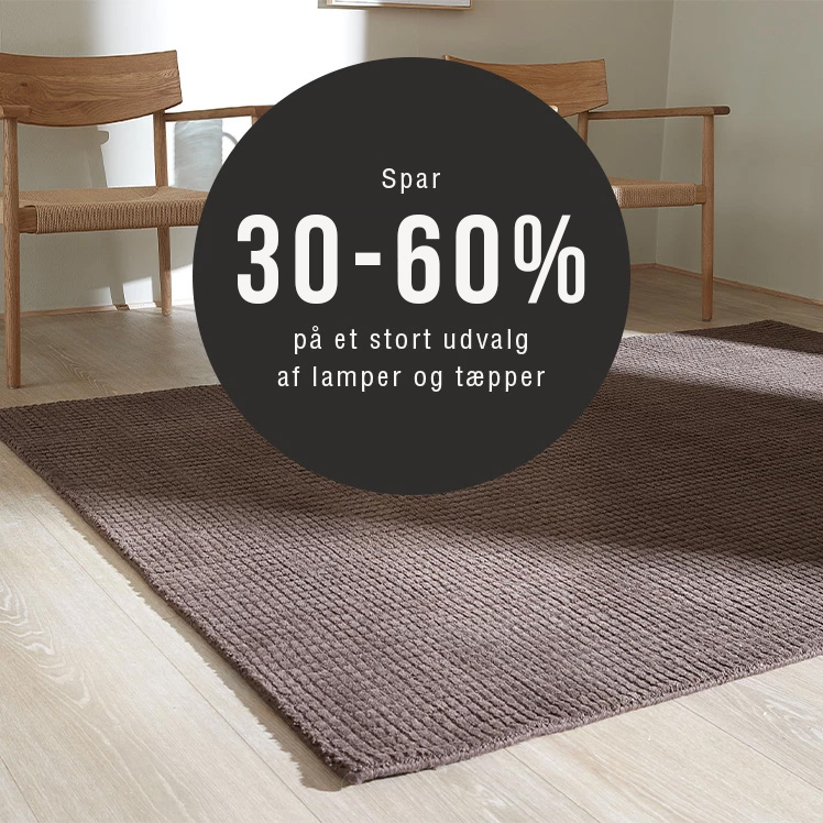 Brun vævet tæppe på lyst trægulv med to træstole i baggrunden – spar 30–60 % på lamper og tæpper.