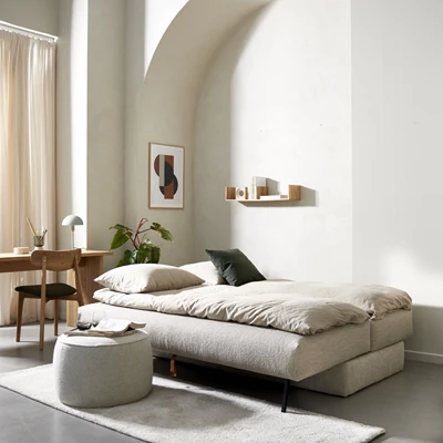 Opredt, lys sovesofa i minimalistisk stue med skrivebord og puf