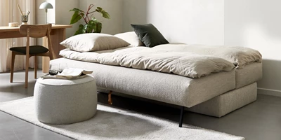 Opredt, lys sovesofa i minimalistisk stue med skrivebord og puf