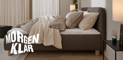 size-210x210.jpg Seng i brun set fra siden med dyner i beige sengetøj liggende ovenpå